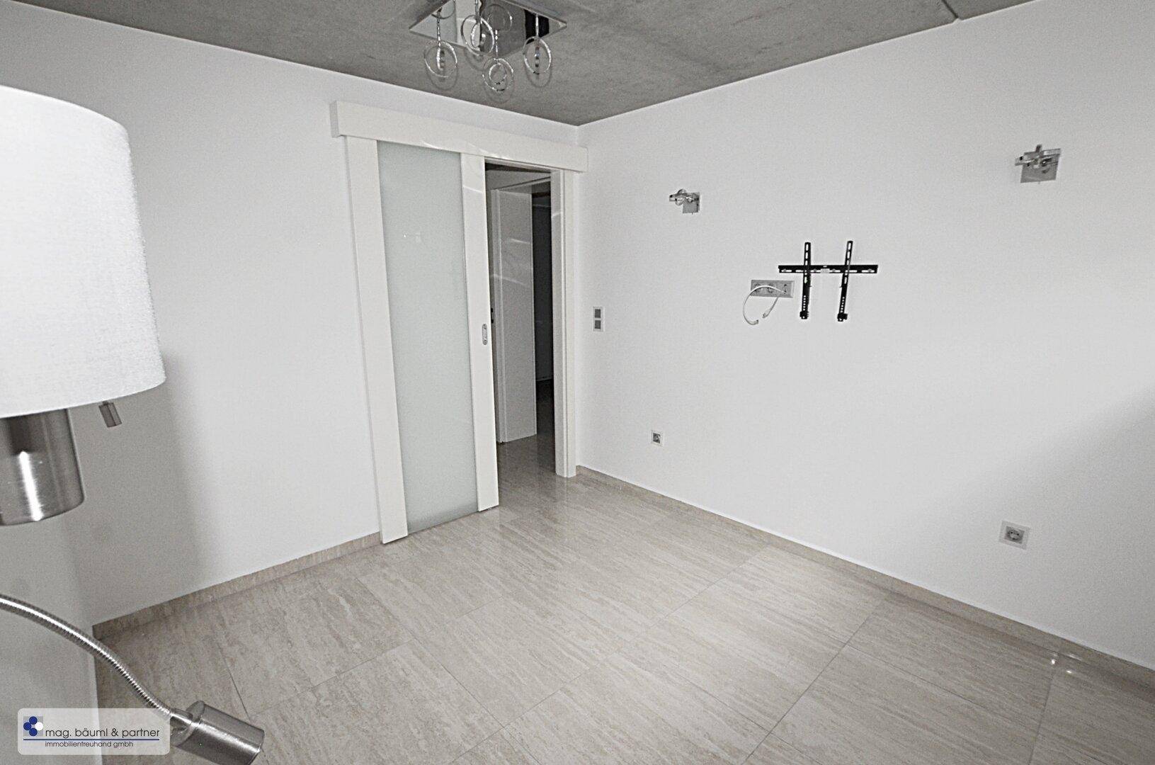 Zimmer im Untergeschoss mit hellen Fliesen und Vorbereitung für Wandmontage eines Fernsehers.