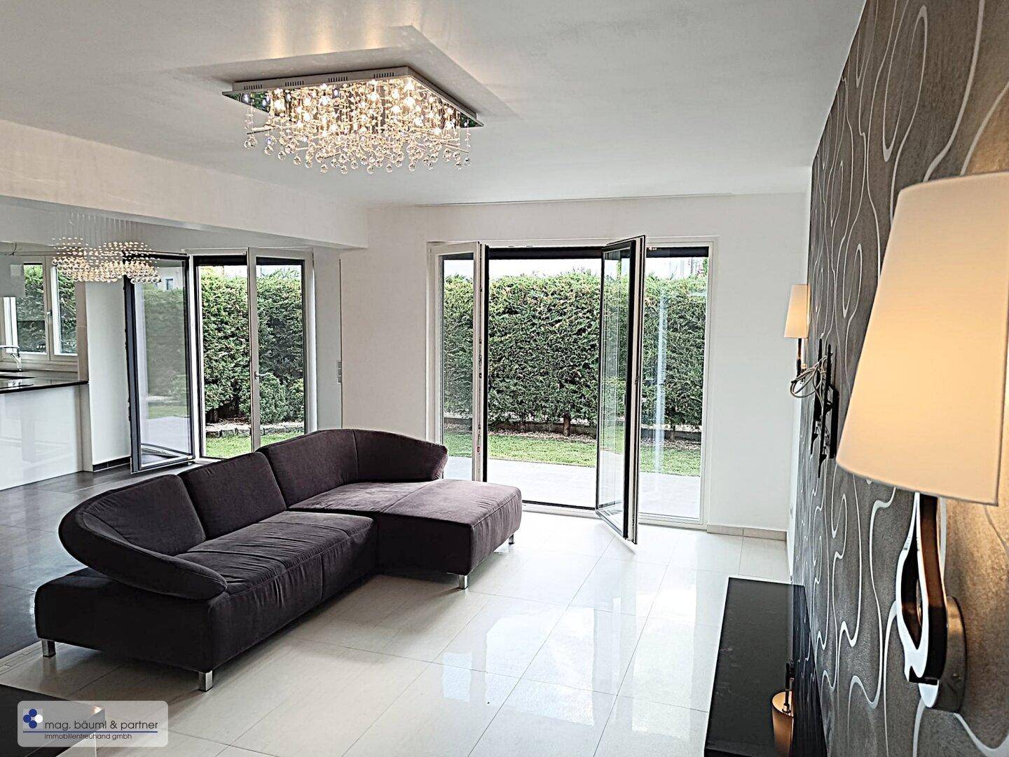 Helles Wohnzimmer mit dunklem Sofa, glänzenden Fliesen und Zugang zum Garten.