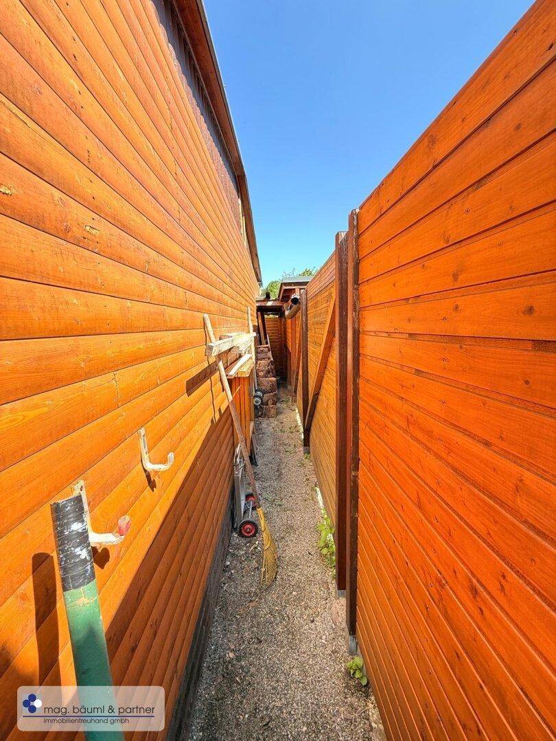 Schmaler Durchgang zwischen zwei Holzzäunen, der Zugang zu weiteren Bereichen ermöglicht.