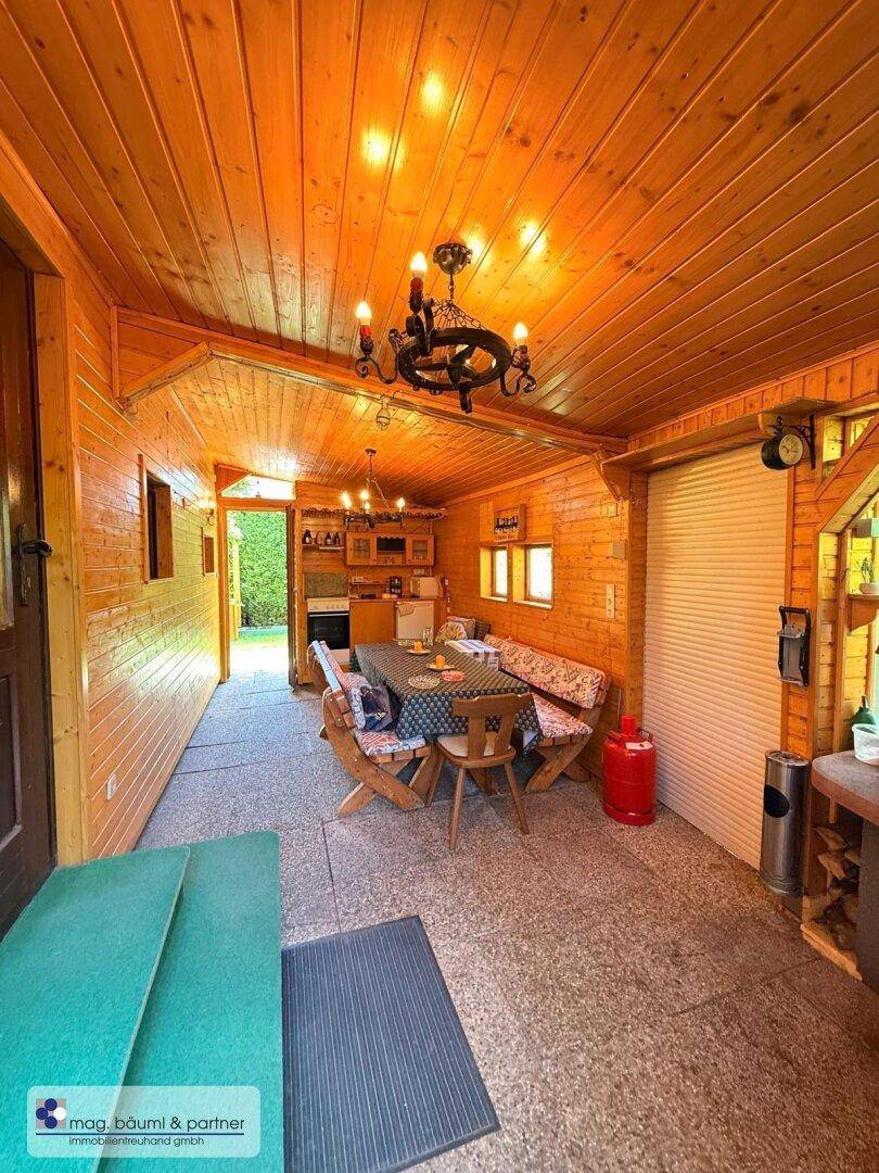 Geräumiger überdachter Terrassenbereich mit Esstisch, Bänken und einer kleinen Küchenzeile im Hintergrund.