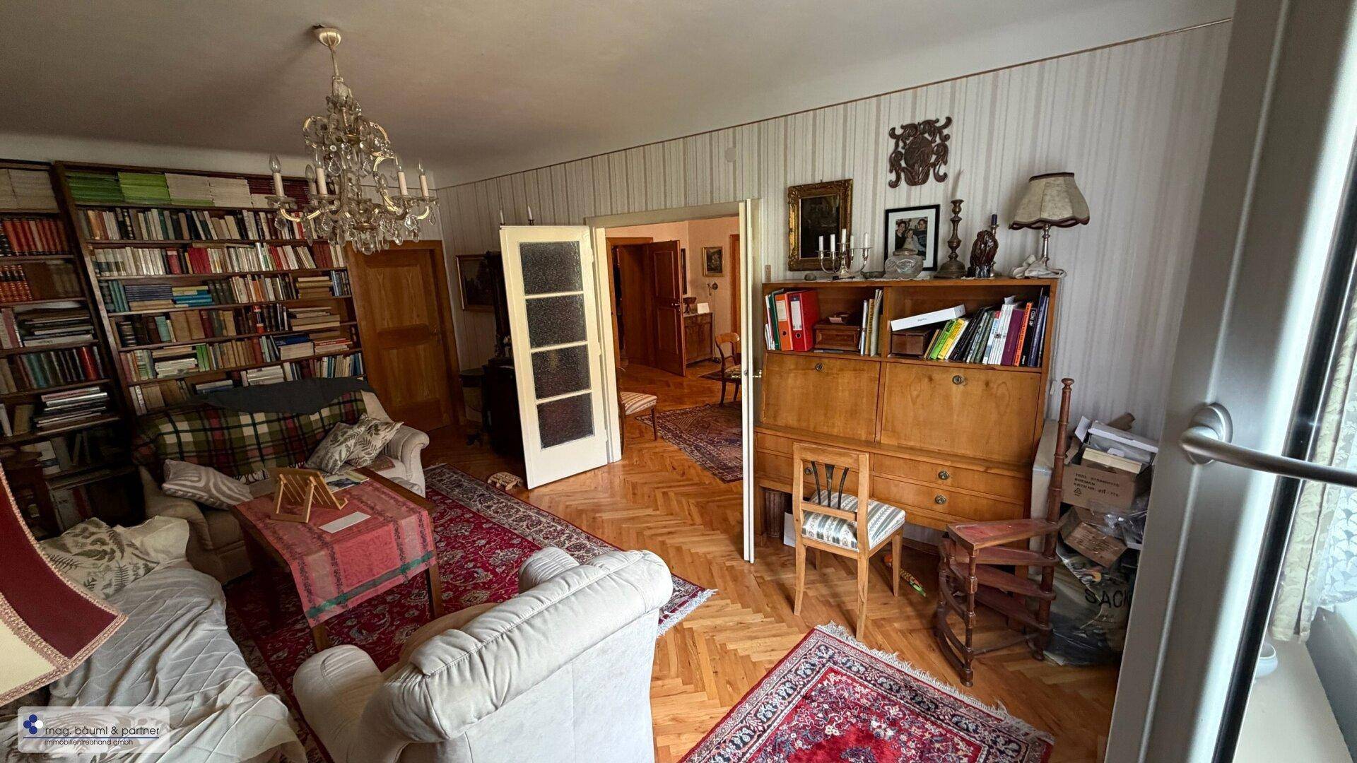 Geräumiges Wohnzimmer mit Parkettboden, Bücherregalen und Kronleuchter.