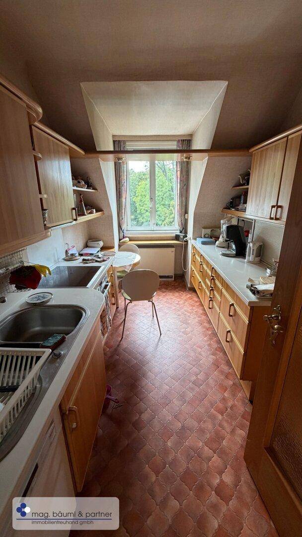 Funktionale Küche mit Dachschräge, Holzschränken und gefliestem Boden.