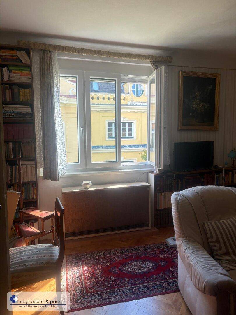 Heller Wohnbereich mit Parkettboden, Bücherregalen und Blick auf die Stadt.