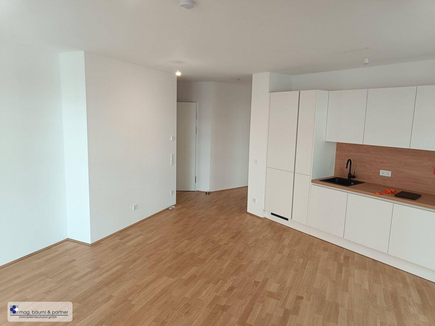Heller Raum mit Holzboden und einer modernen weißen Küchenzeile.