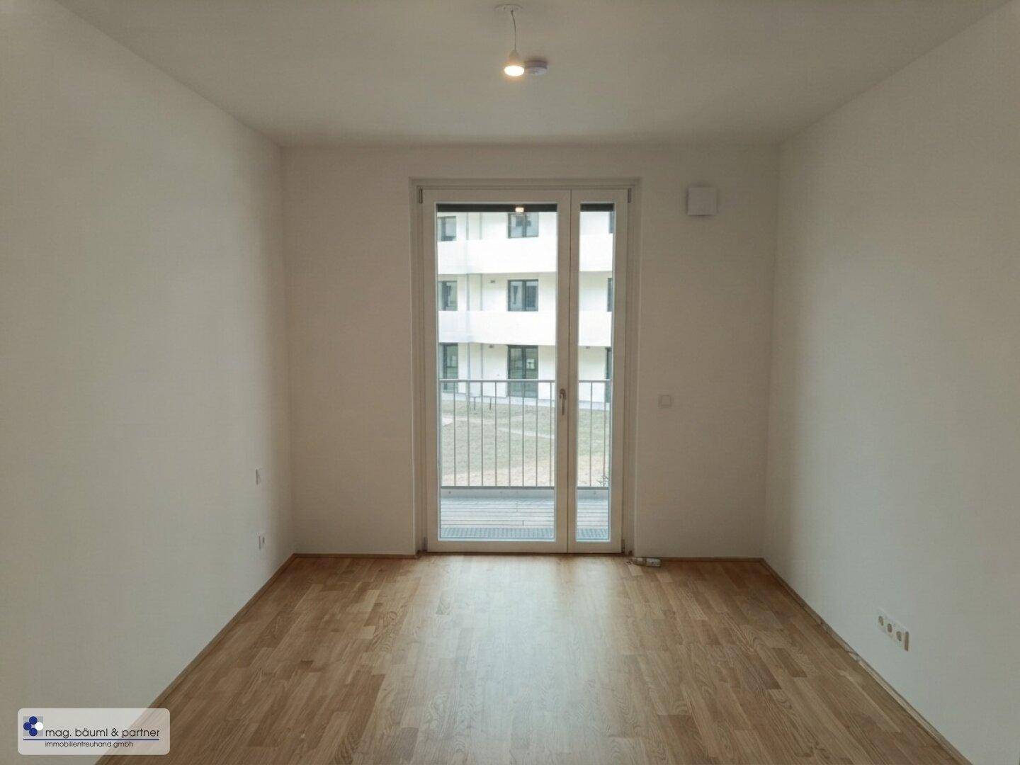 Freundliches Zimmer mit Holzboden und Balkonzugang, ideal als Schlaf- oder Arbeitszimmer.