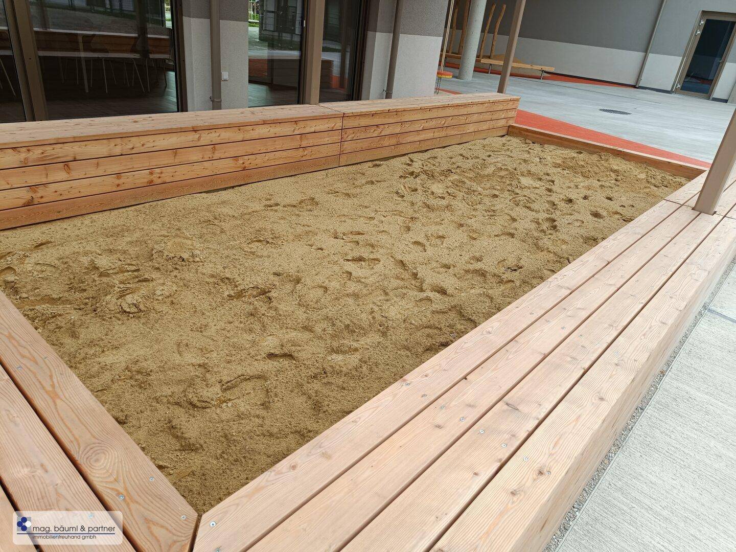 Detailansicht eines Sandkastens mit Holzumrandung im gemeinschaftlichen Spielbereich.