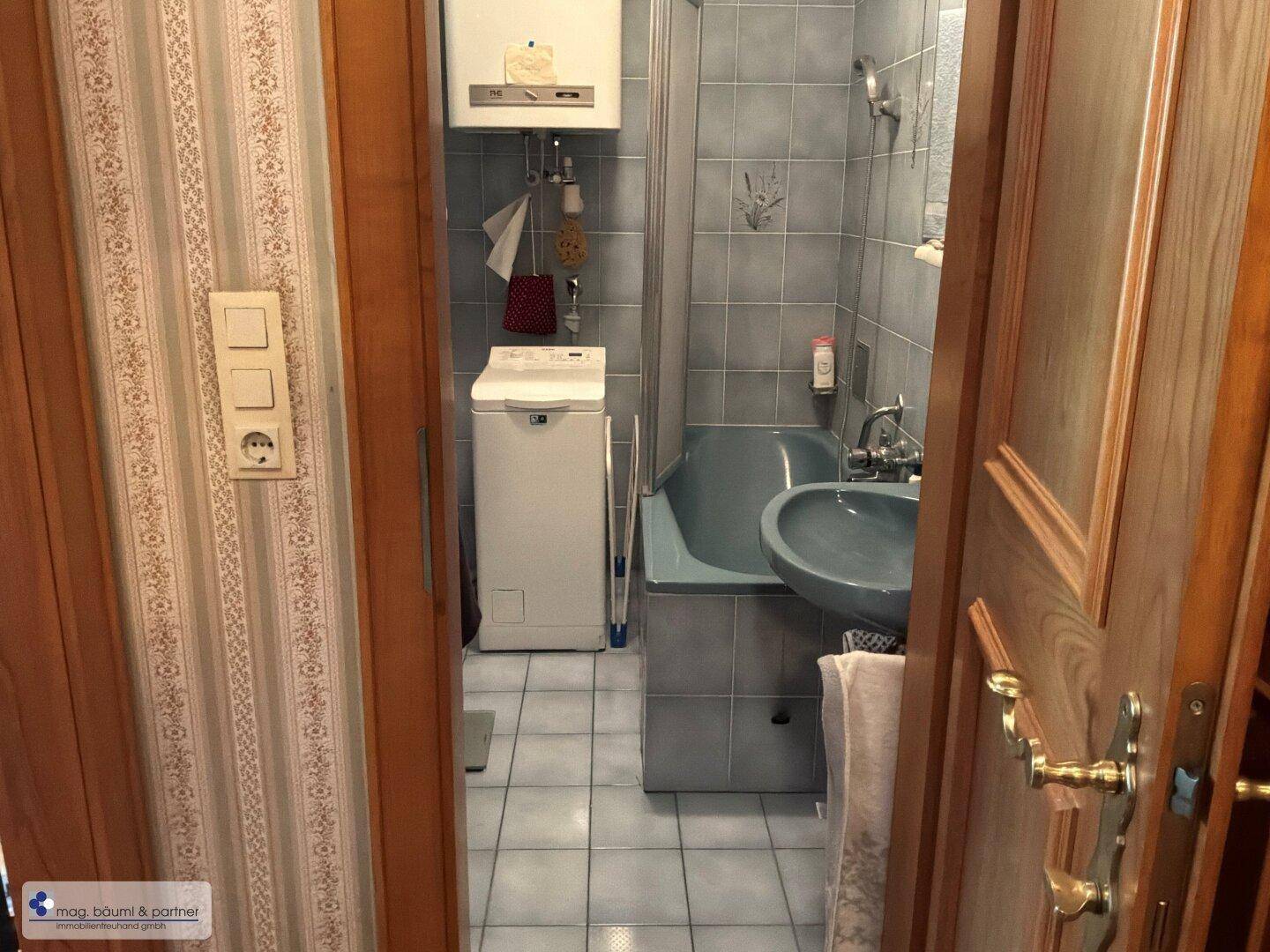 Kleines Badezimmer mit Dusche, Waschbecken und Waschmaschine.