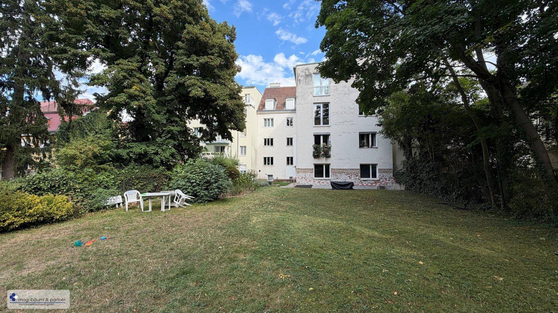 Großer Gemeinschaftsgarten mit Rasenfläche und Sitzgelegenheiten hinter dem Gebäude.