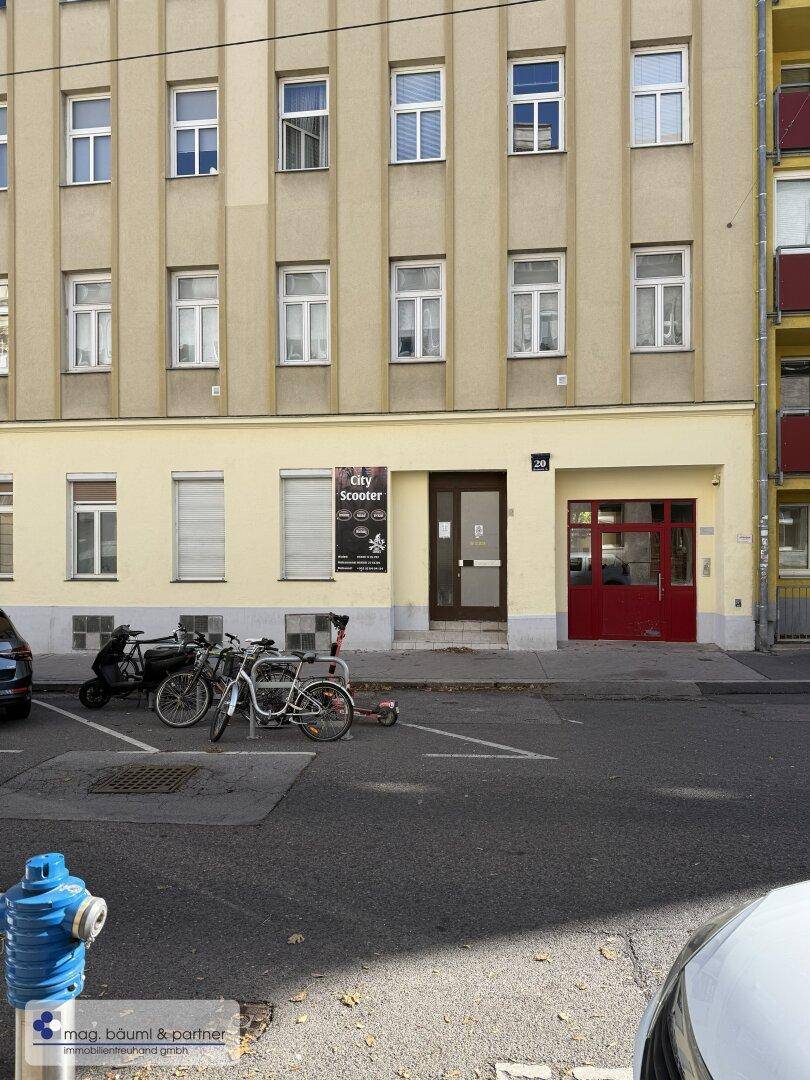 Fassade eines Mehrfamilienhauses mit Eingangsbereich und parkenden Fahrzeugen.