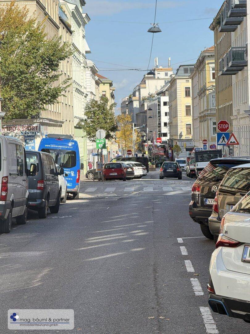 Ruhige Wohnstraße mit parkenden Autos und Gebäuden unter blauem Himmel.