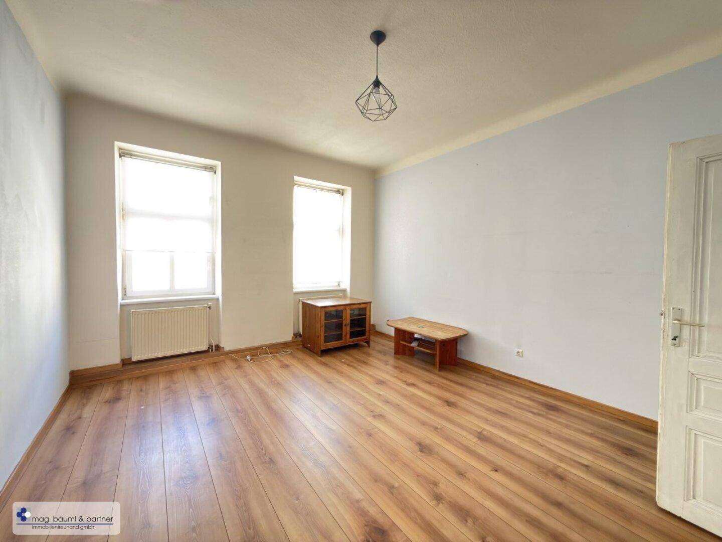 Geräumiges Schlafzimmer mit Holzboden, zwei Fenstern und hellblauen Wänden.
