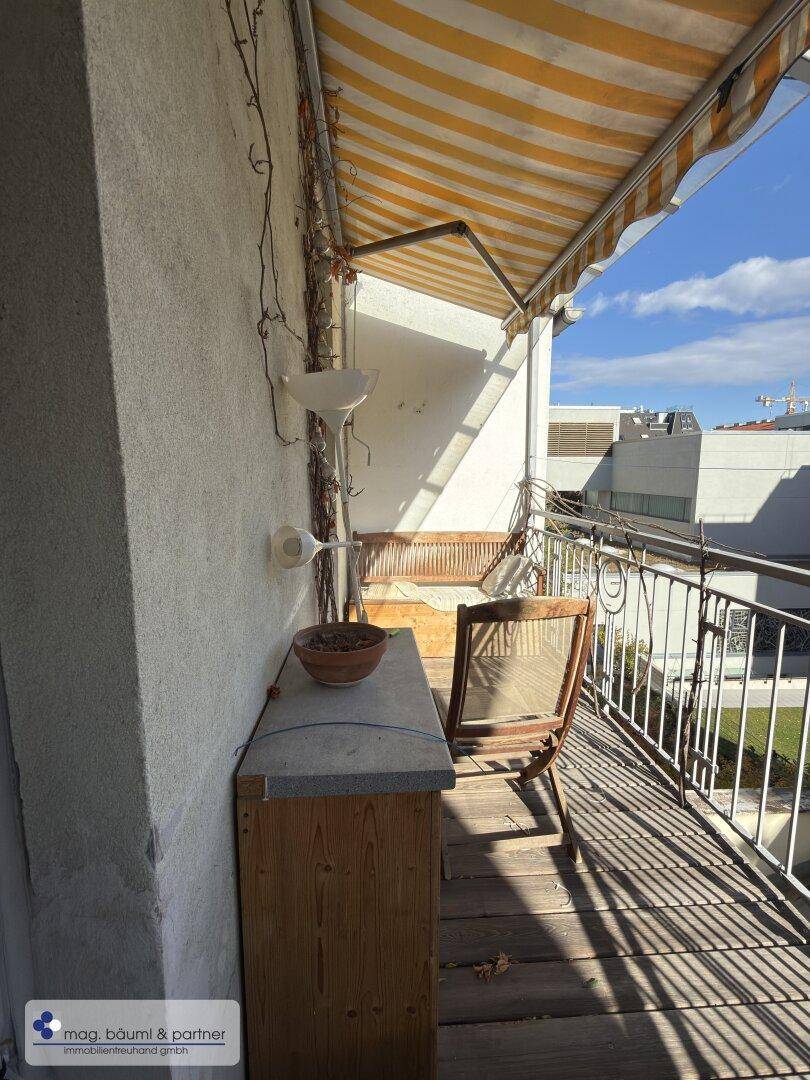 Sonniger Balkon mit Markise, Holzboden und Blick auf die Umgebung.