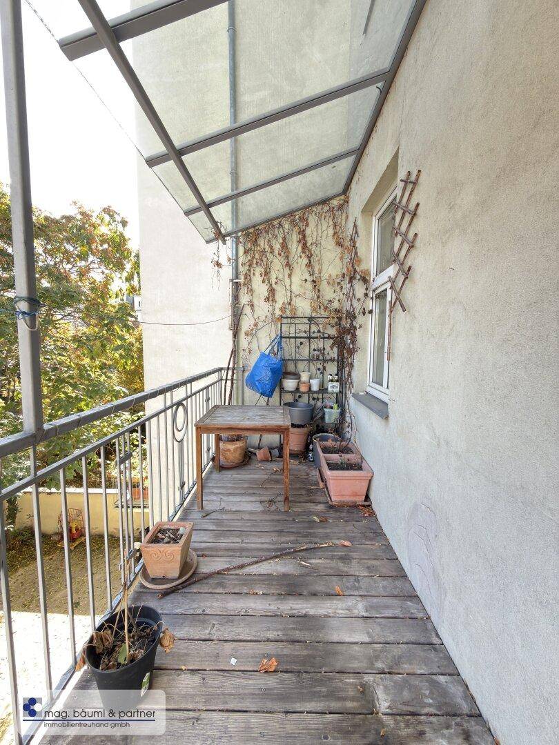 Überdachter Balkon mit Holzboden, Pflanzen und Blick ins Grüne.