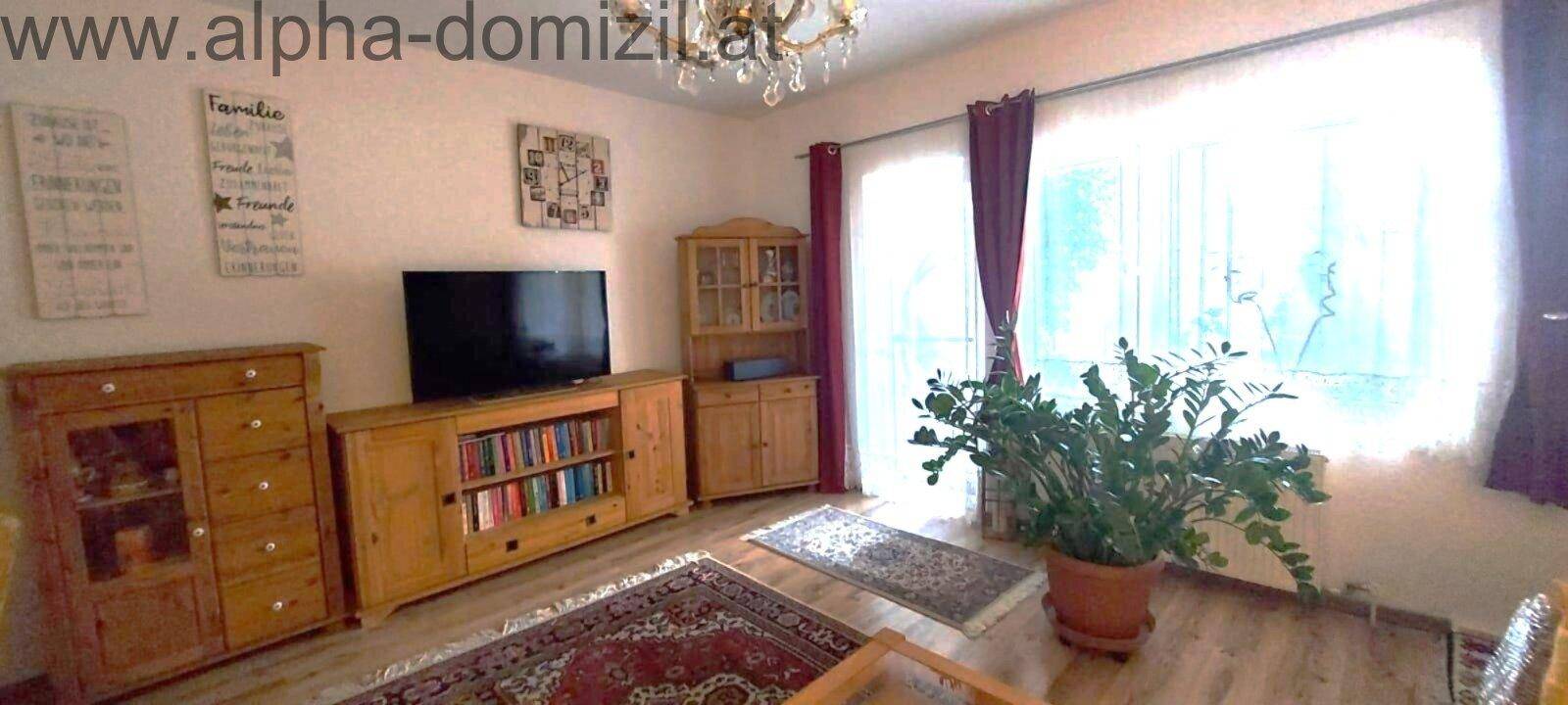 Helles Wohnzimmer mit großen Fenstern, Holzboden und traditionellen Holzmöbeln.