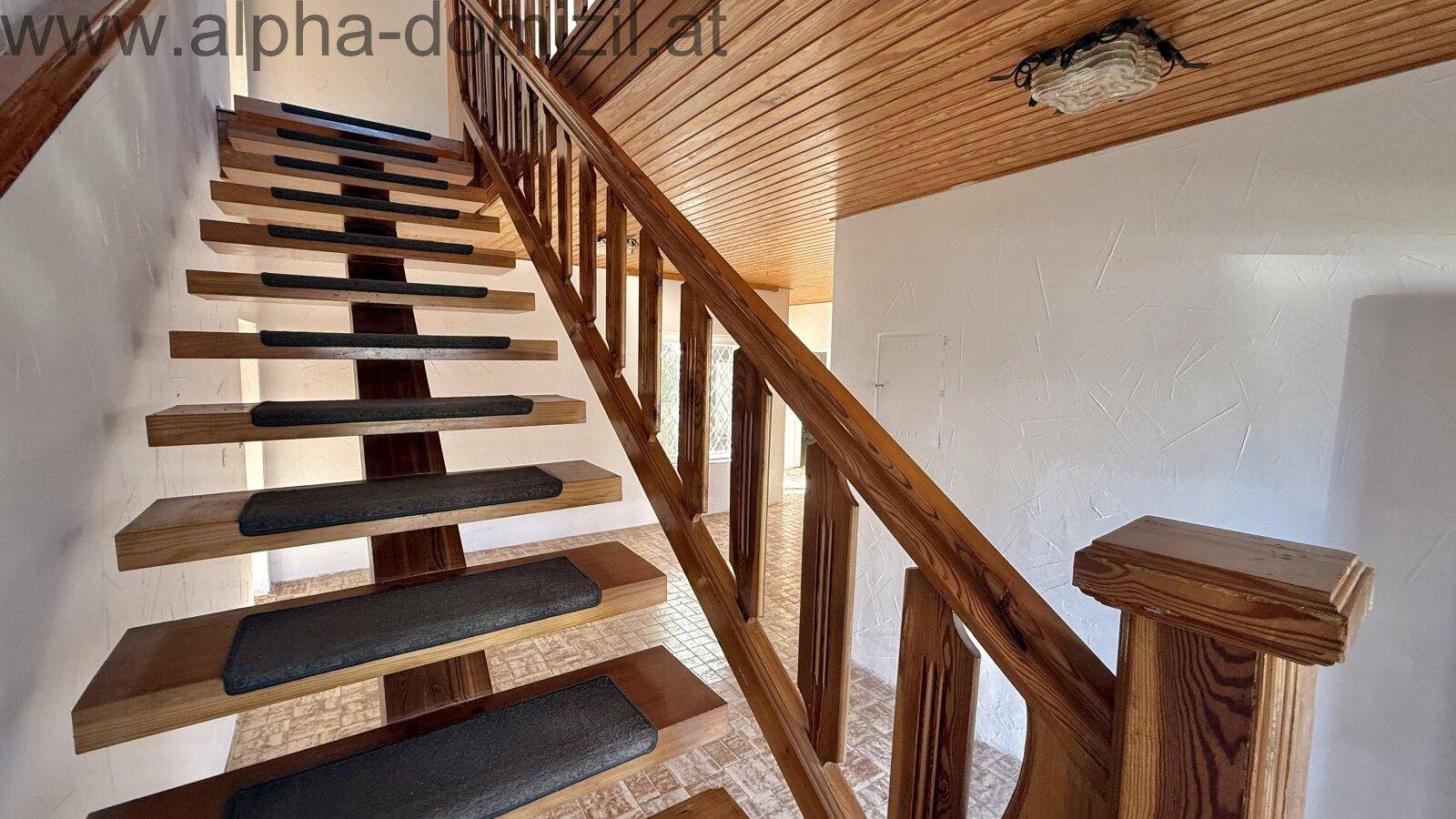 Detailansicht einer massiven Holztreppe mit Teppichauflagen und einer passenden Holzdeckenverkleidung.