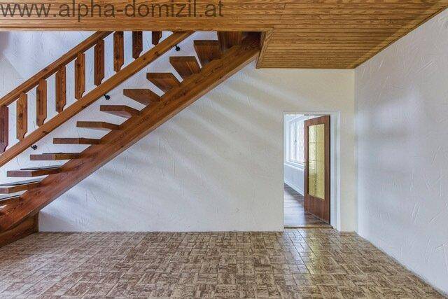 Eingangsbereich mit Holztreppe und gemustertem Fliesenboden, der zu einem weiteren Raum führt.