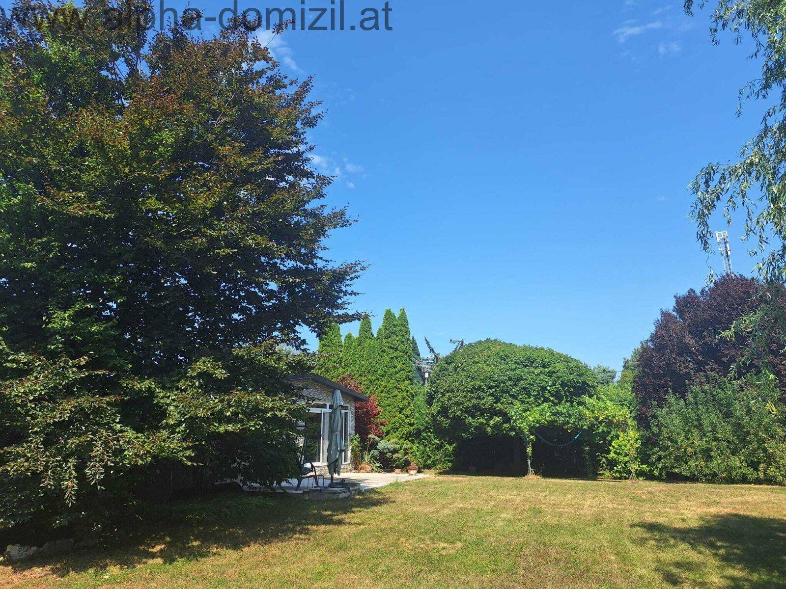 Großer, gepflegter Garten mit altem Baumbestand und Blick auf die Rückseite des Hauses.