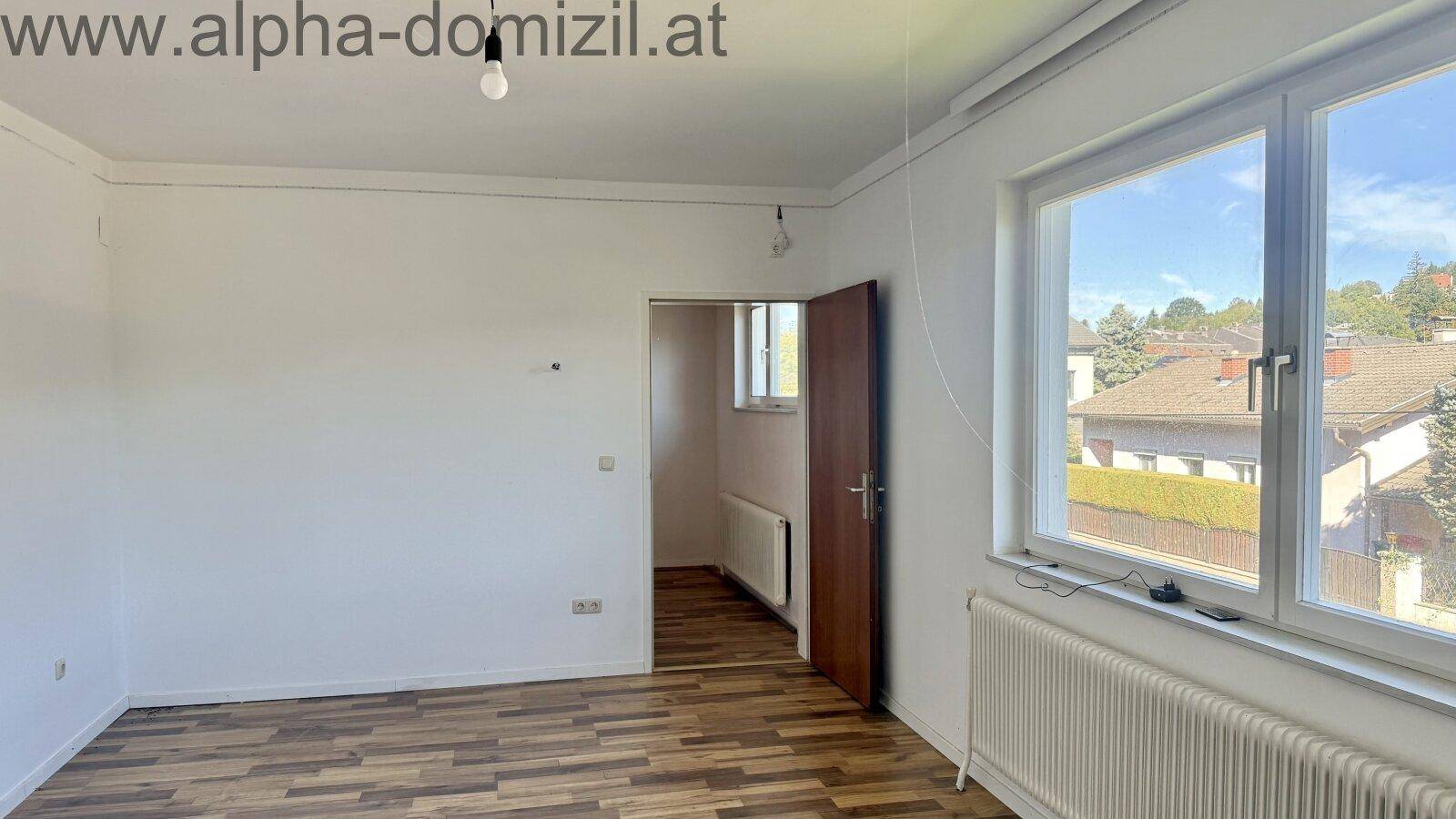 Heller Raum mit Laminatboden und großem Fenster, das einen Blick nach draußen ermöglicht.