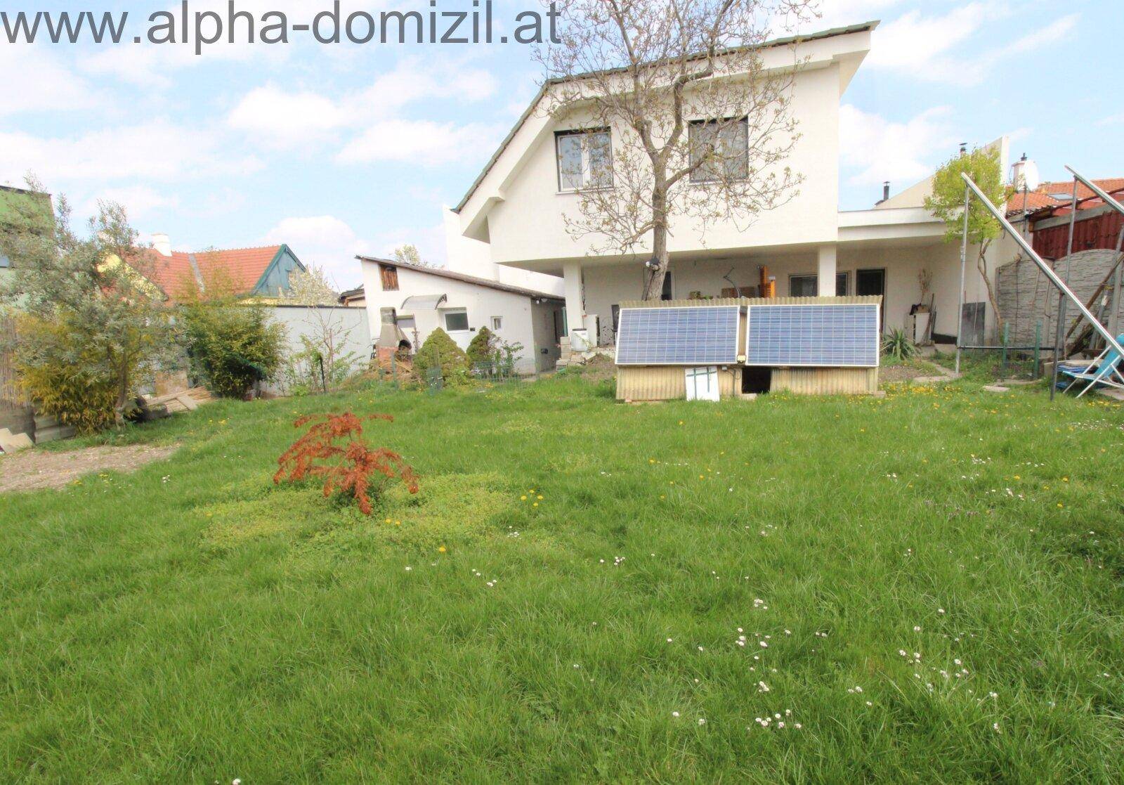 Großer Garten mit Rasenfläche und einem modernen Haus im Hintergrund, ausgestattet mit Solarpaneelen.