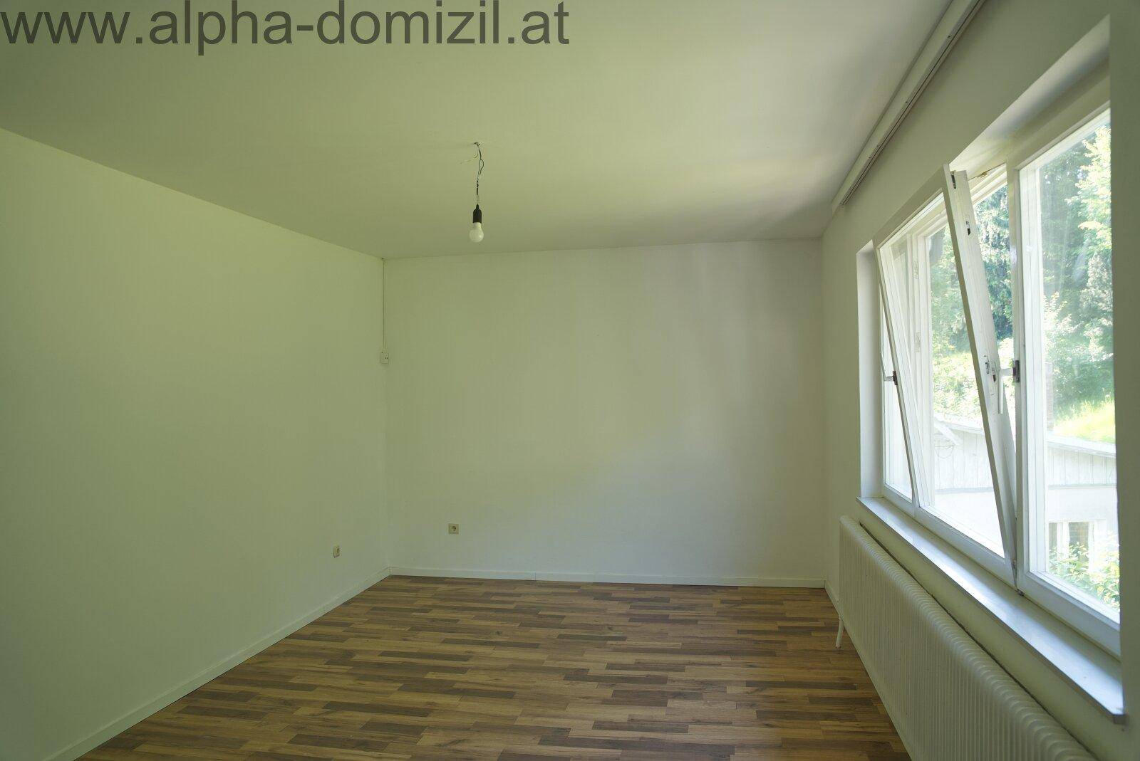 Helles Schlafzimmer mit Laminatboden und großen Fenstern, die viel Tageslicht hereinlassen.