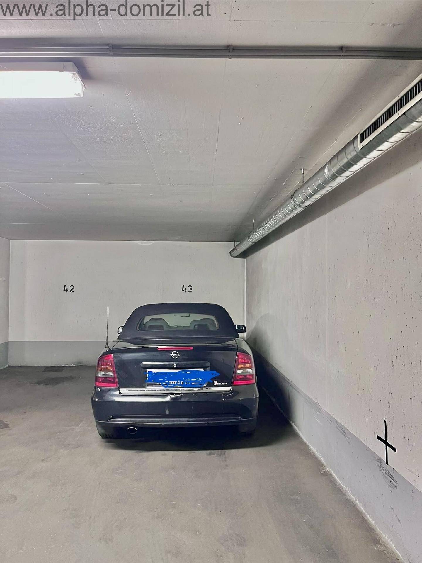 Geräumiger Tiefgaragenstellplatz mit robusten Betonwänden und sichtbaren Lüftungsrohren an der Decke.