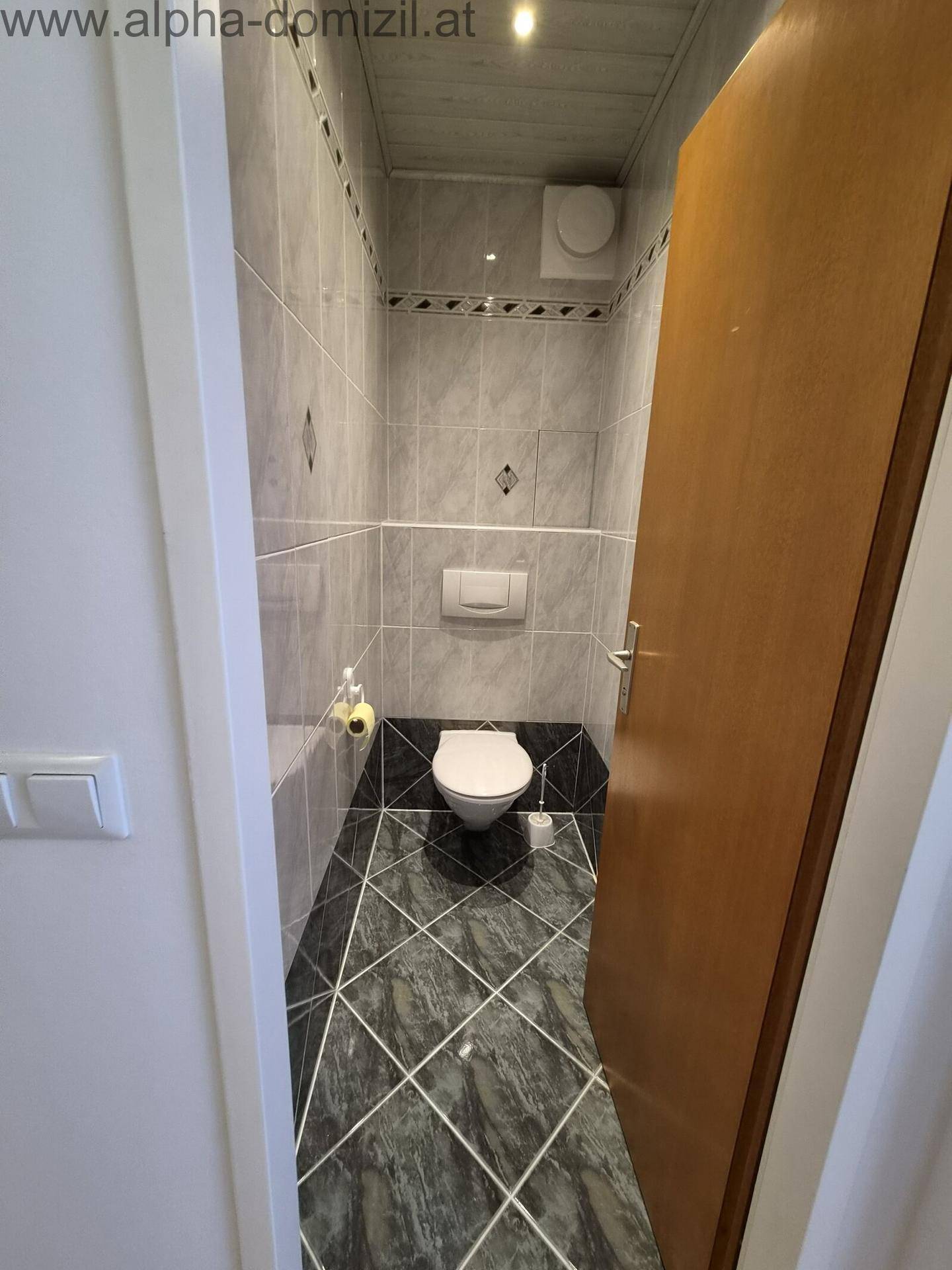 Kleines Gäste-WC mit Wand-WC und dunklen Fliesen am Boden und an den Wänden.