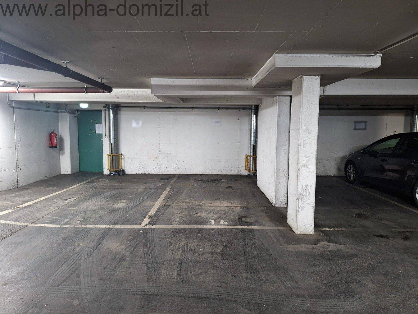 Leerer Bereich einer Tiefgarage mit markierten Stellplätzen und Brandschutzvorrichtung.