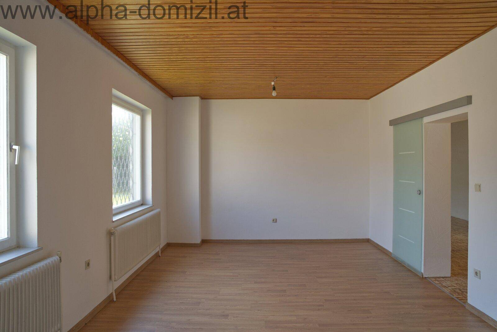 Helles Zimmer mit Laminatboden, Holzdecke und einer modernen Glasschiebetür.