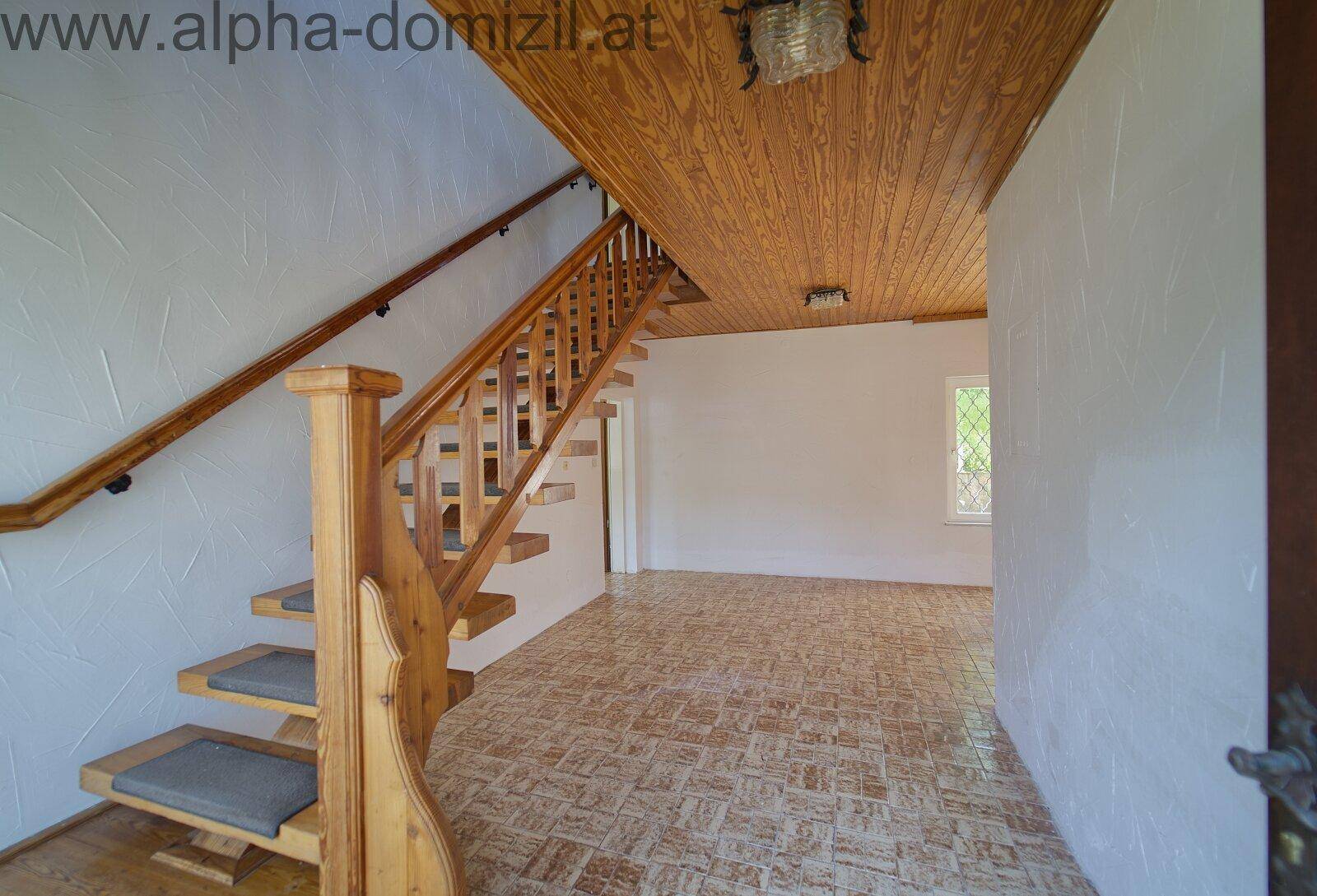 Geräumiger Flur mit einer Holztreppe, Holzdeckenverkleidung und gemusterten Fliesenboden.