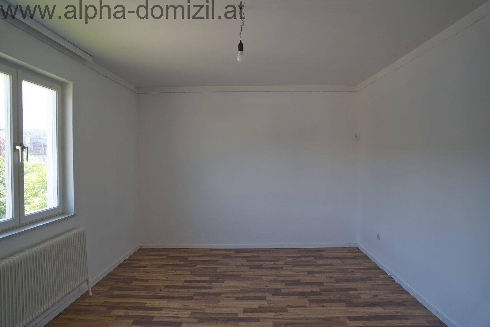 Leeres Zimmer mit Laminatboden und Fenster, bereit zur individuellen Gestaltung.