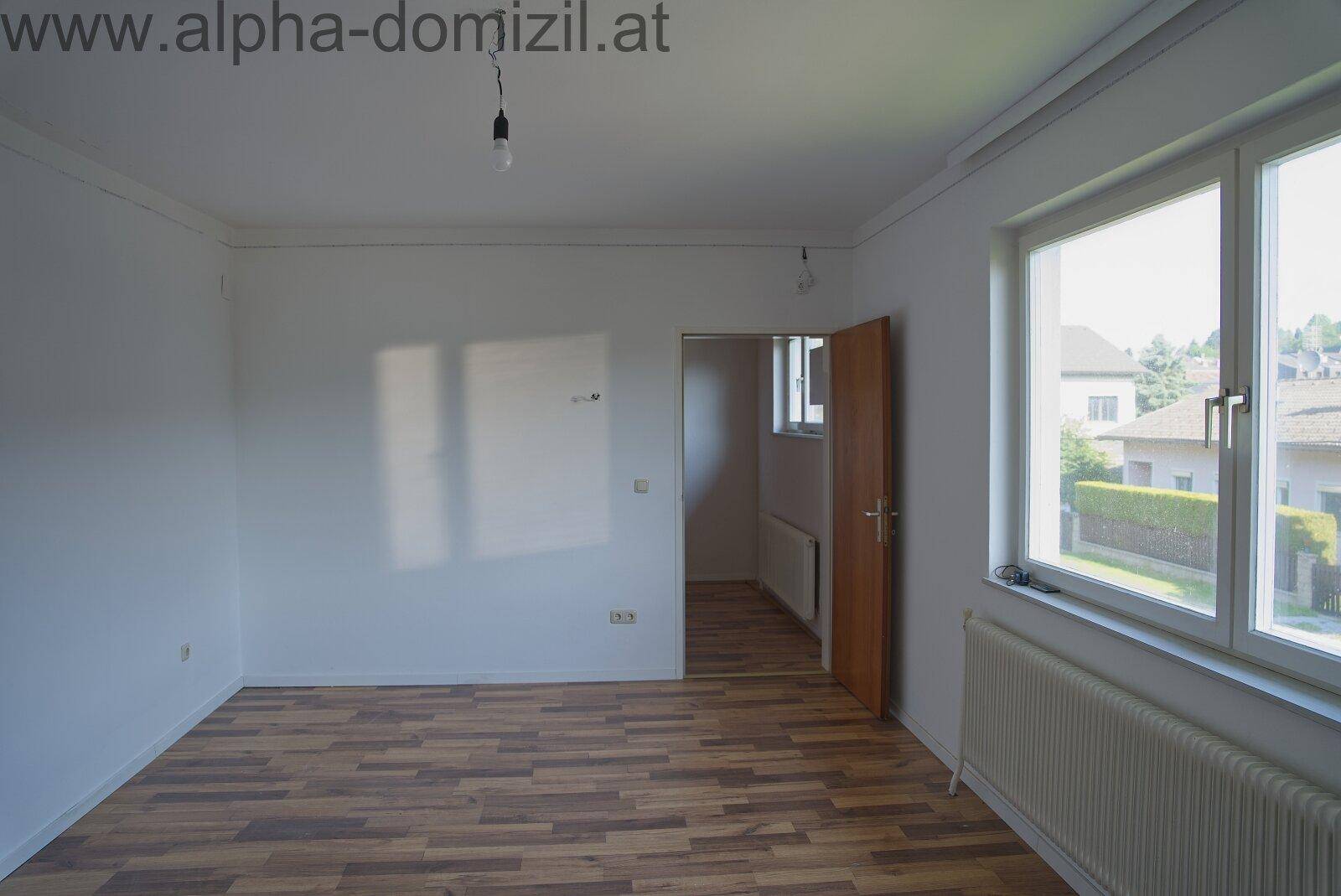 Geräumiges Zimmer mit Laminatboden und Blick ins Grüne durch das Fenster.