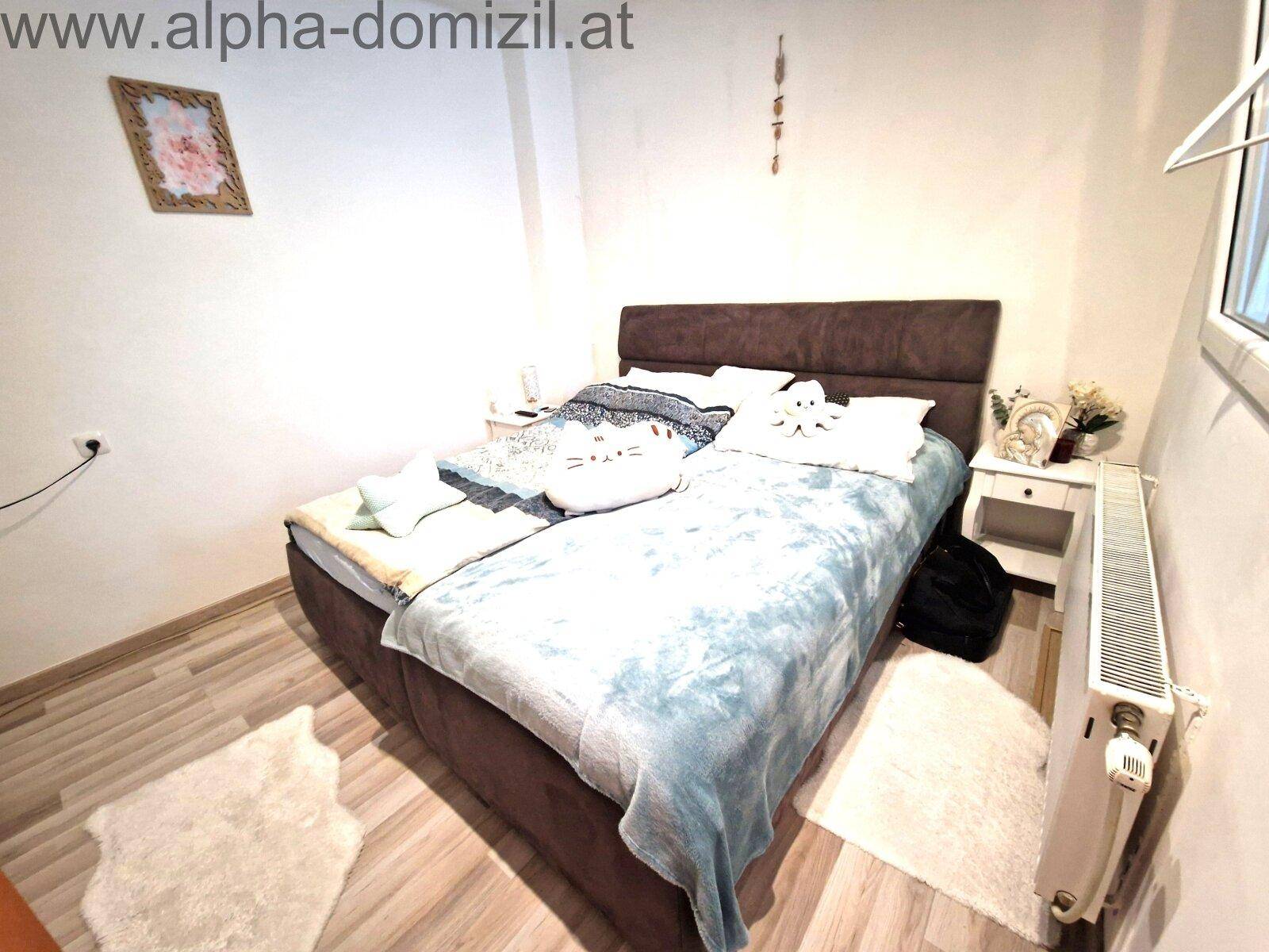 Schlafzimmer mit Doppelbett, hellem Laminatboden und Heizkörper unter dem Fenster.