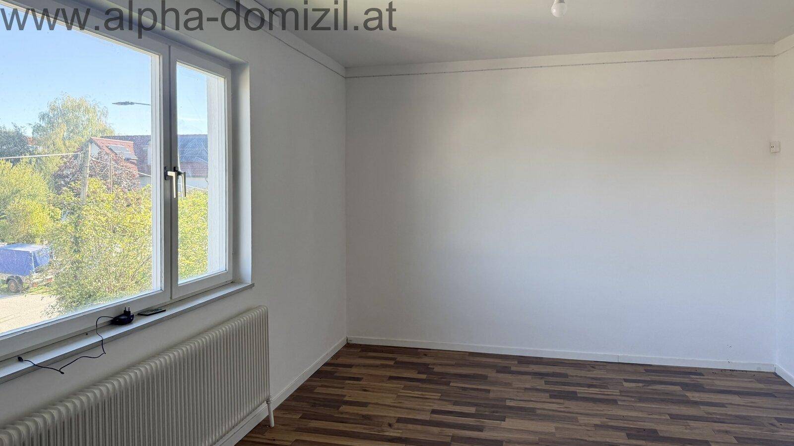 Leerer Raum mit Laminatboden und großem Fenster, das einen Blick auf Bäume und die Umgebung bietet.