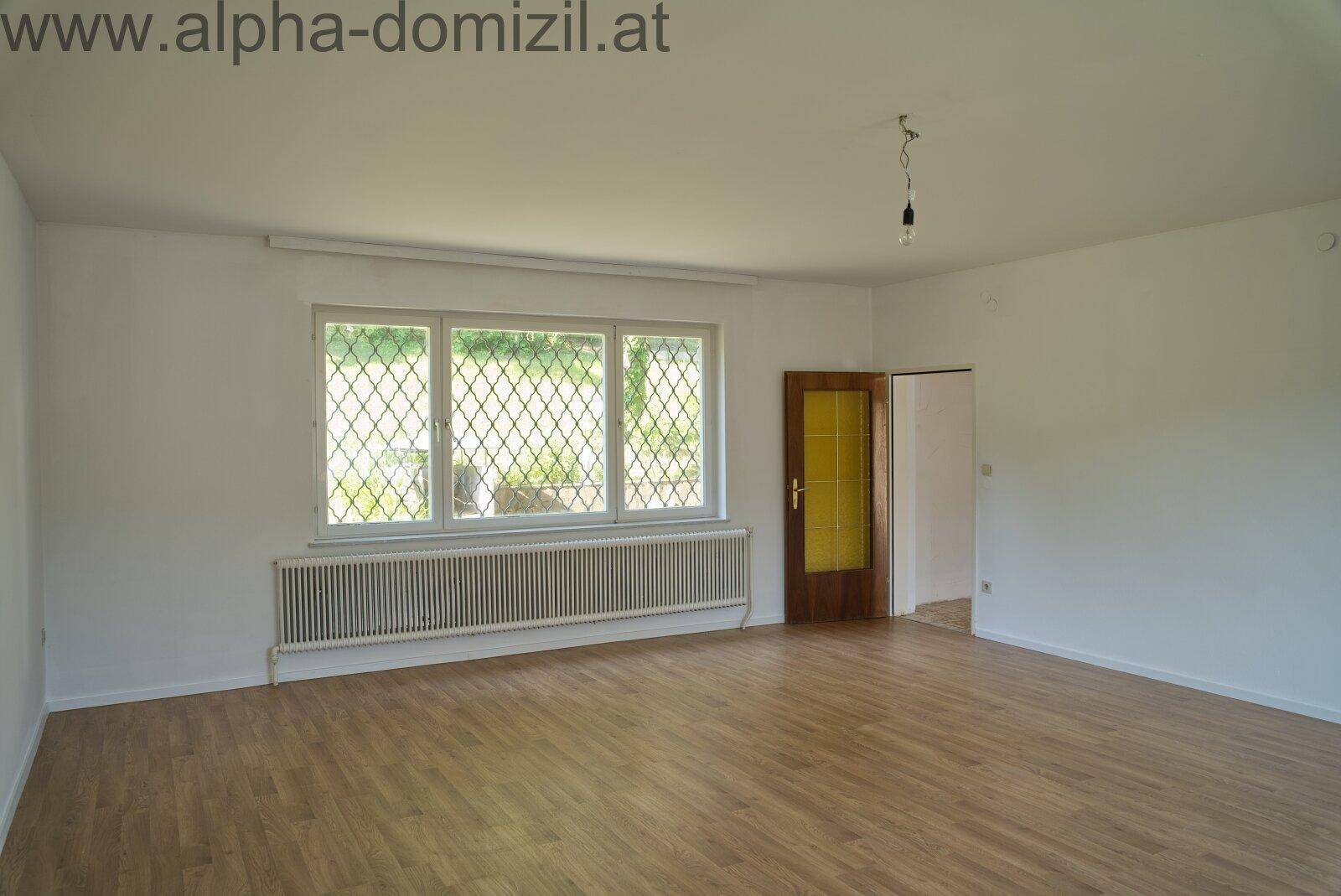 Heller Wohnraum mit Holzboden und drei Fenstern, die viel Tageslicht spenden.