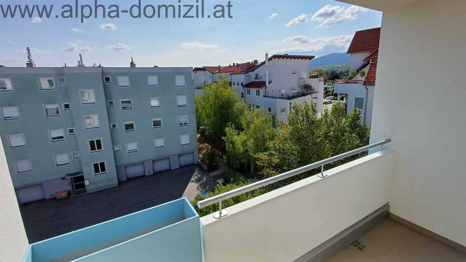 Sonniger Balkon mit Blick auf die umliegenden Gebäude und grüne Hügel in der Ferne.