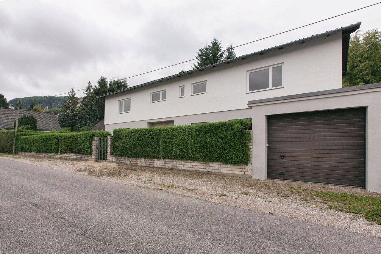 Hausfassade von der Straße aus gesehen mit integrierter Garage und gepflegter Hecke.