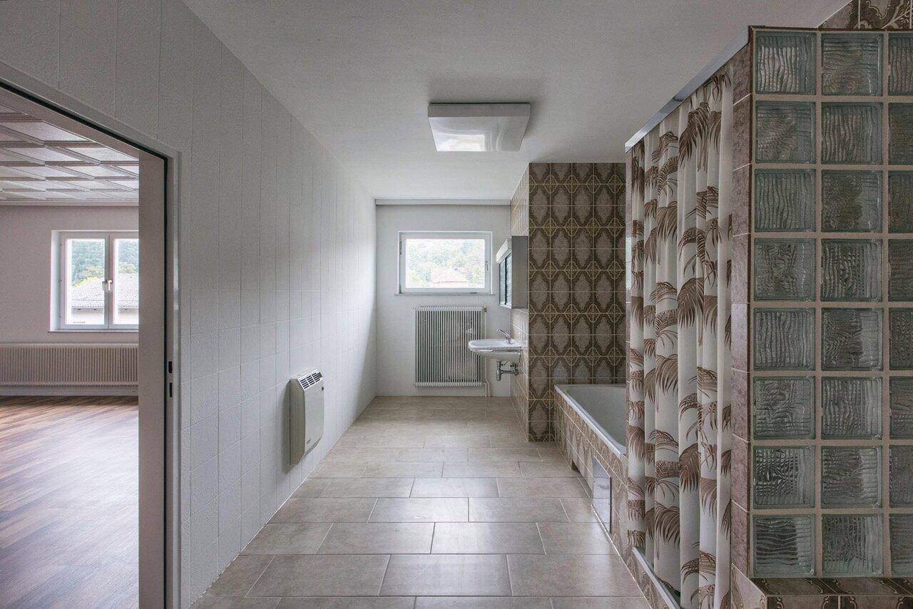 Langes Badezimmer mit Waschbecken, Badewanne und gemusterten Fliesen, die einen Retro-Charme verleihen.
