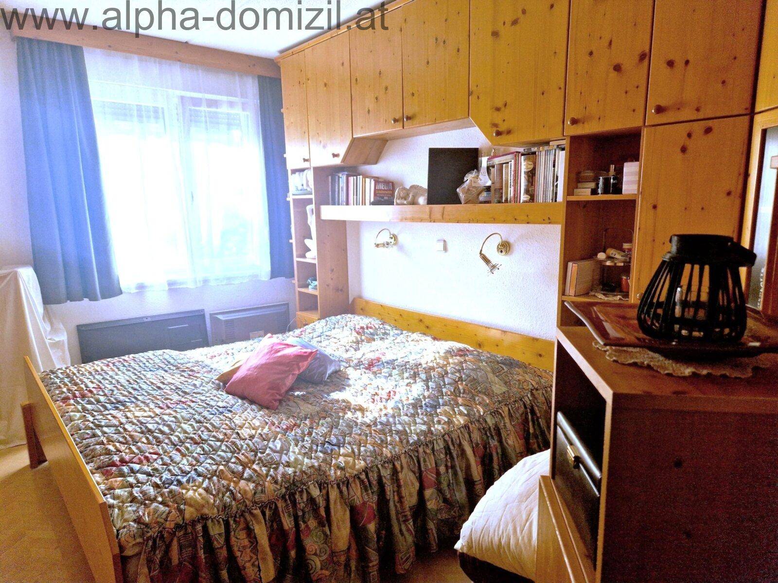 Schlafzimmer mit Holzbett, integrierten Schränken und einem Fenster mit blauen Vorhängen.