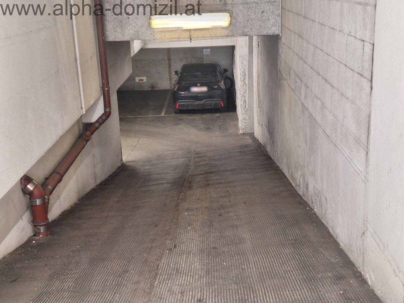 Abfahrt zur Tiefgarage mit geriffelter Rampe und sichtbaren Rohren.
