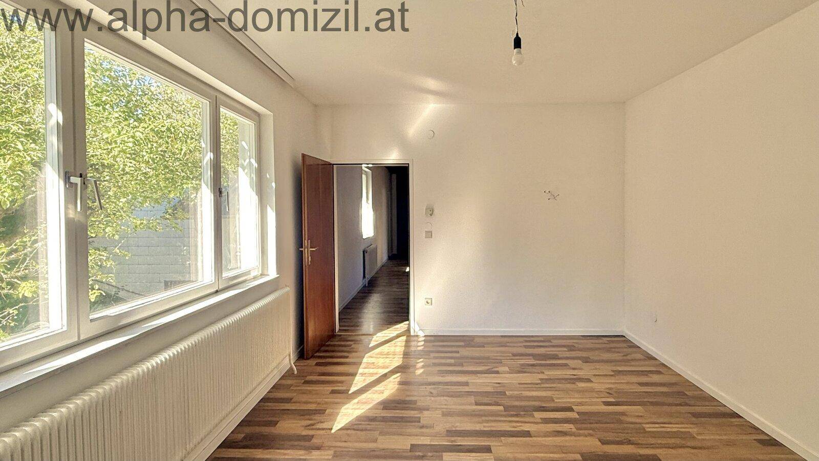 Lichtdurchfluteter Raum mit Laminatboden und großem Fenster, durch das die Sonne scheint.