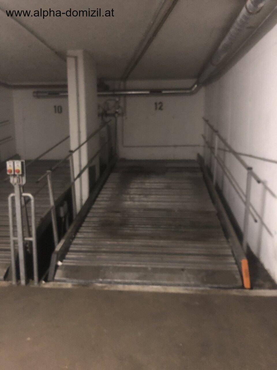 Zufahrtsrampe zu einer Tiefgarage mit nummerierten Stellplätzen und Geländern.