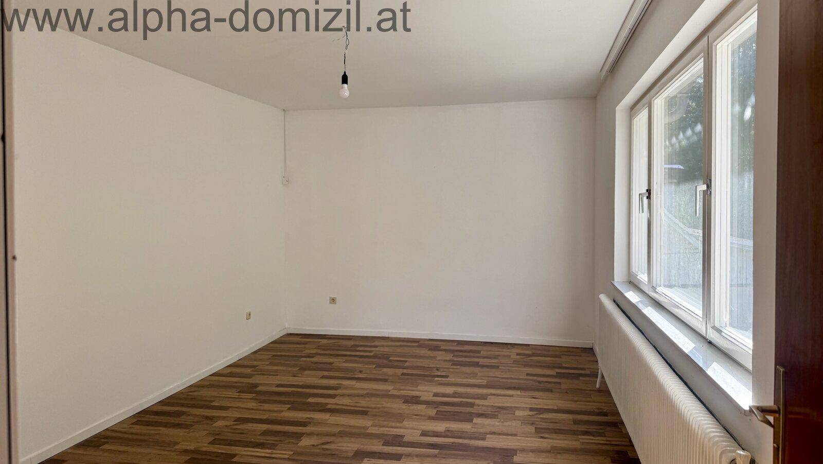 Geräumiger, leerer Raum mit Laminatboden und einem großen Fenster, das für Helligkeit sorgt.