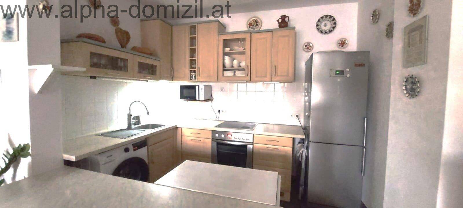 Funktionale Küche mit Holzschränken, integriertem Backofen und Waschmaschine.