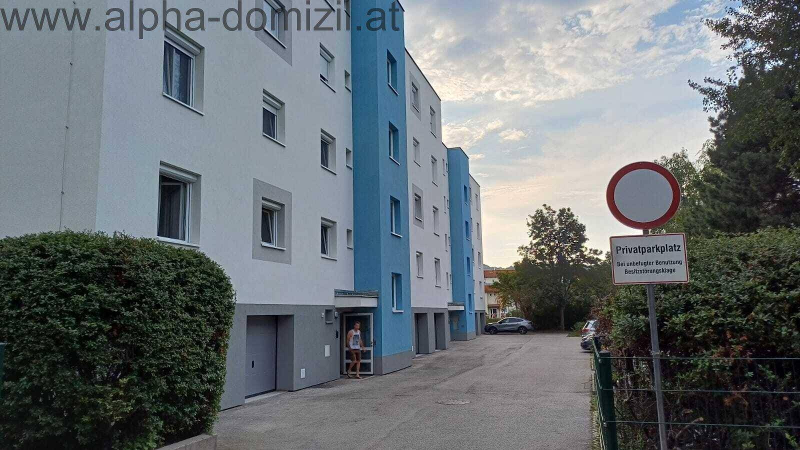Mehrfamilienhaus mit blauen Akzenten und Privatparkplatz im Freien unter bewölktem Himmel.