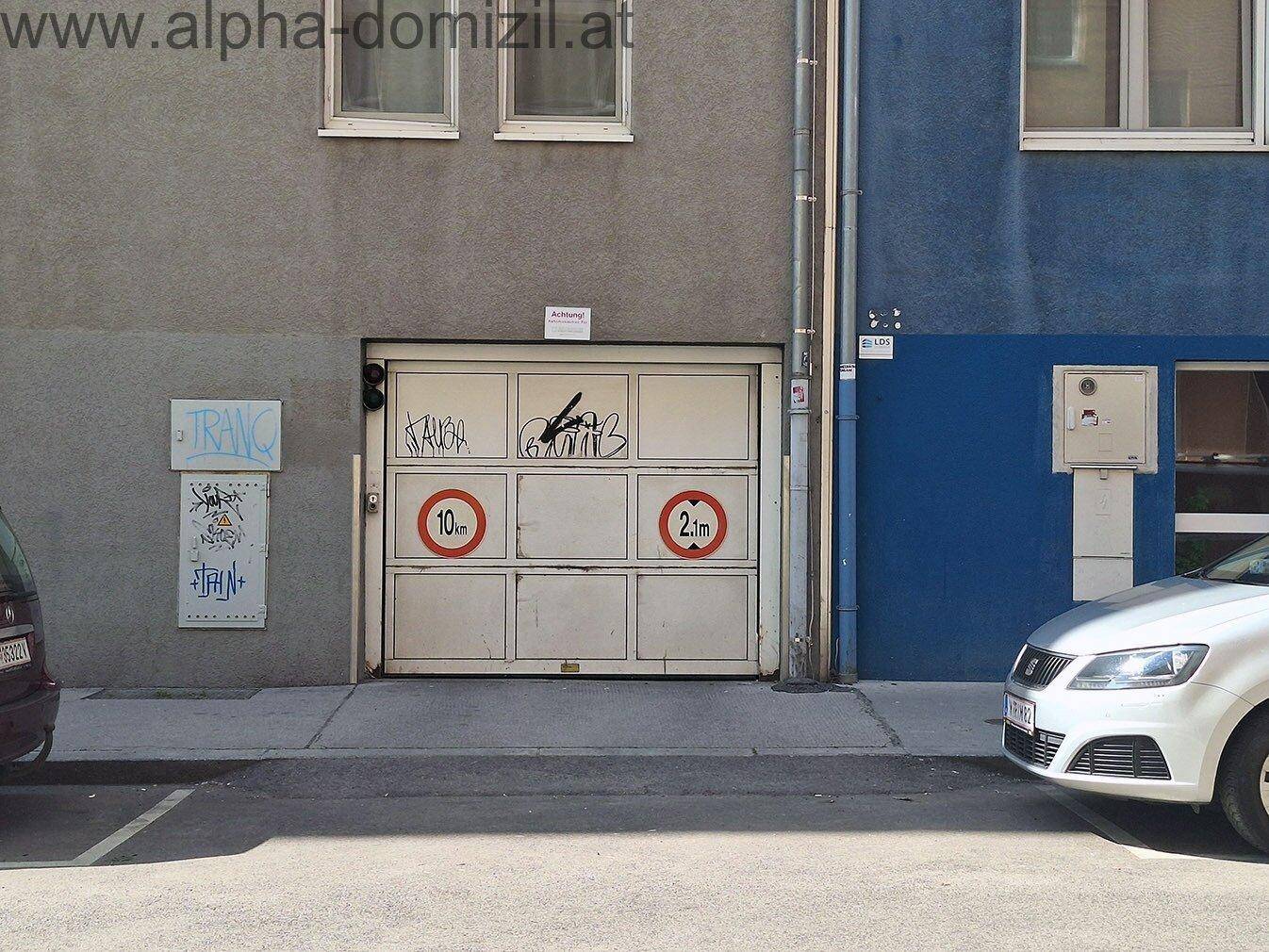 Geschlossene Tiefgarageneinfahrt mit Graffiti und Höhenbegrenzungsschildern an der Fassade.