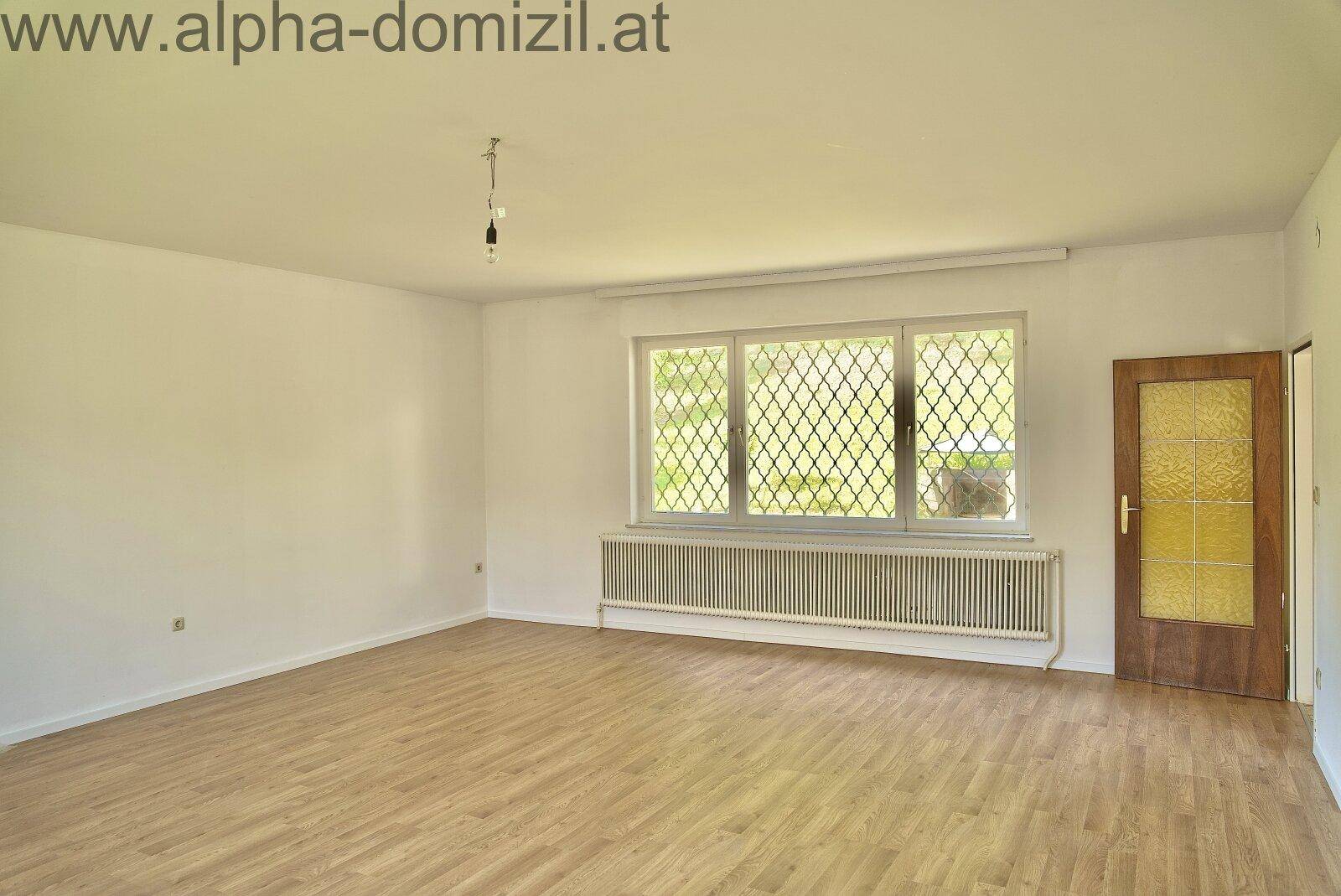 Heller, leerer Raum mit Laminatboden und einem großen Fenster mit dekorativem Gitter, bereit zur Gestaltung.