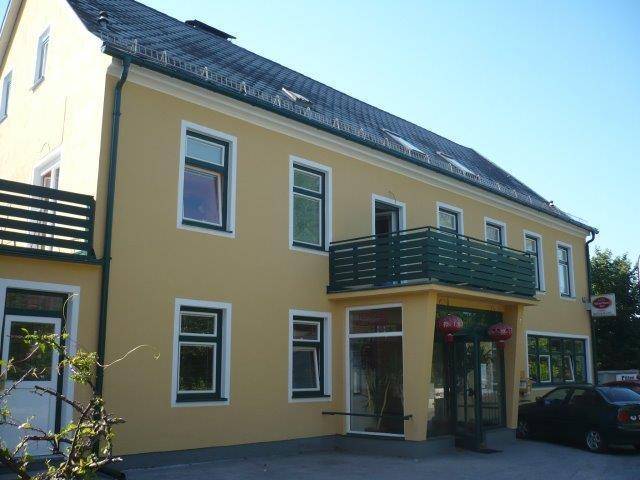 Gelbe Gebäudefassade mit mehreren Balkonen und dunklen Fensterrahmen an einem sonnigen Tag.