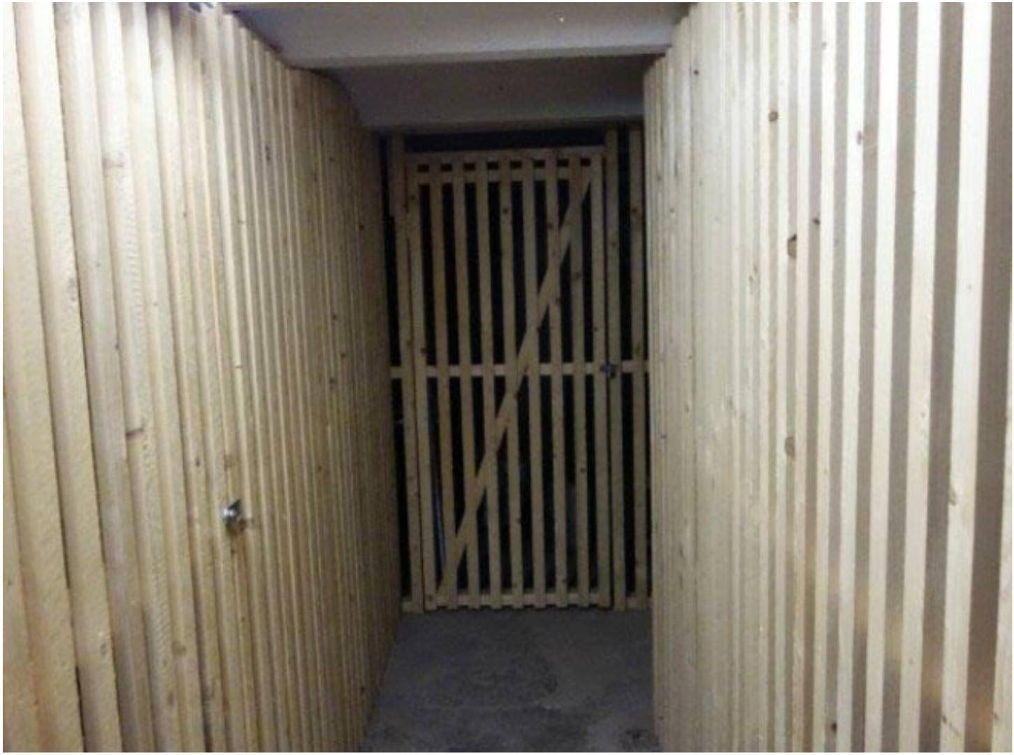 Schmaler Gang mit Holzlattenwänden, der zu einem Lagerabteil im Keller führt.
