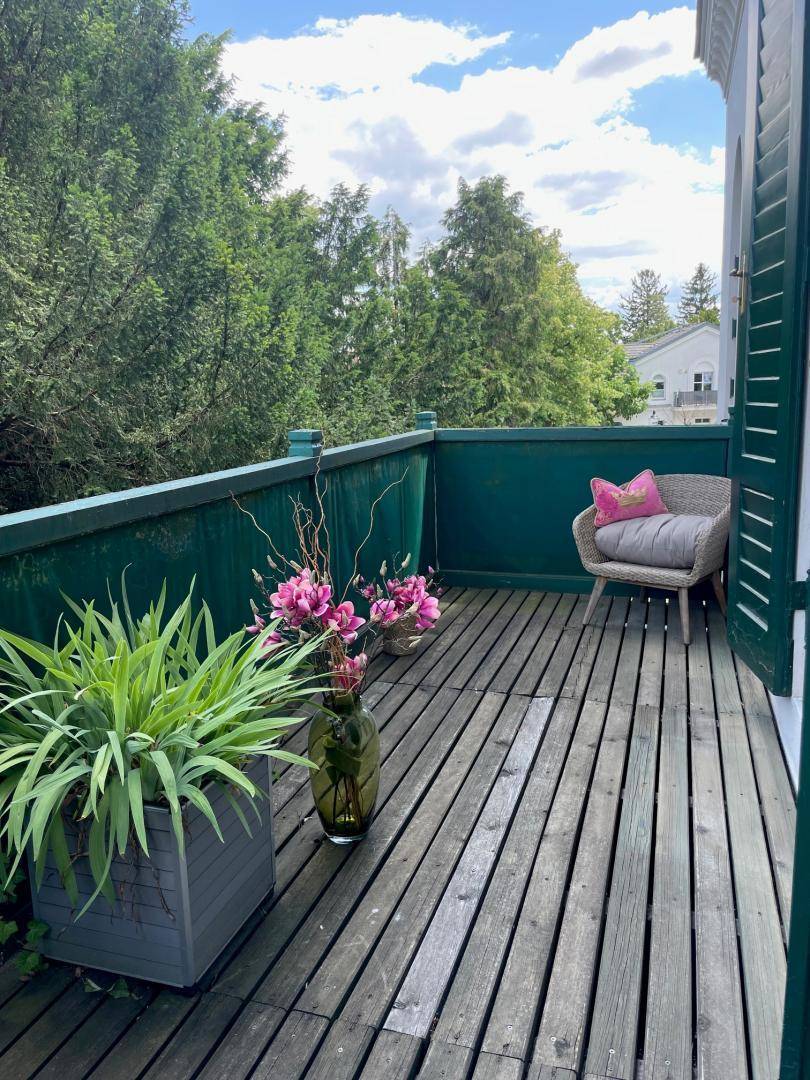 Gemütlicher Balkon mit Holzboden, bequemen Sitzmöbeln und üppigen Pflanzen, umgeben von viel Grün.