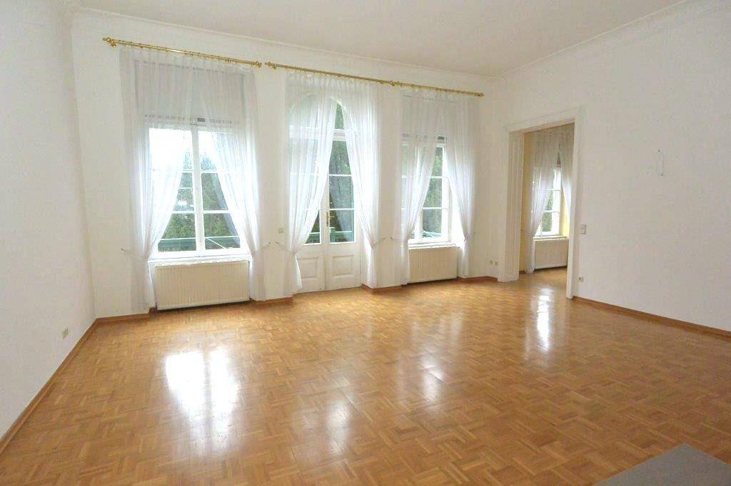 Geräumiges Wohnzimmer mit hellem Parkettboden, hohen Fenstern und viel Tageslicht.